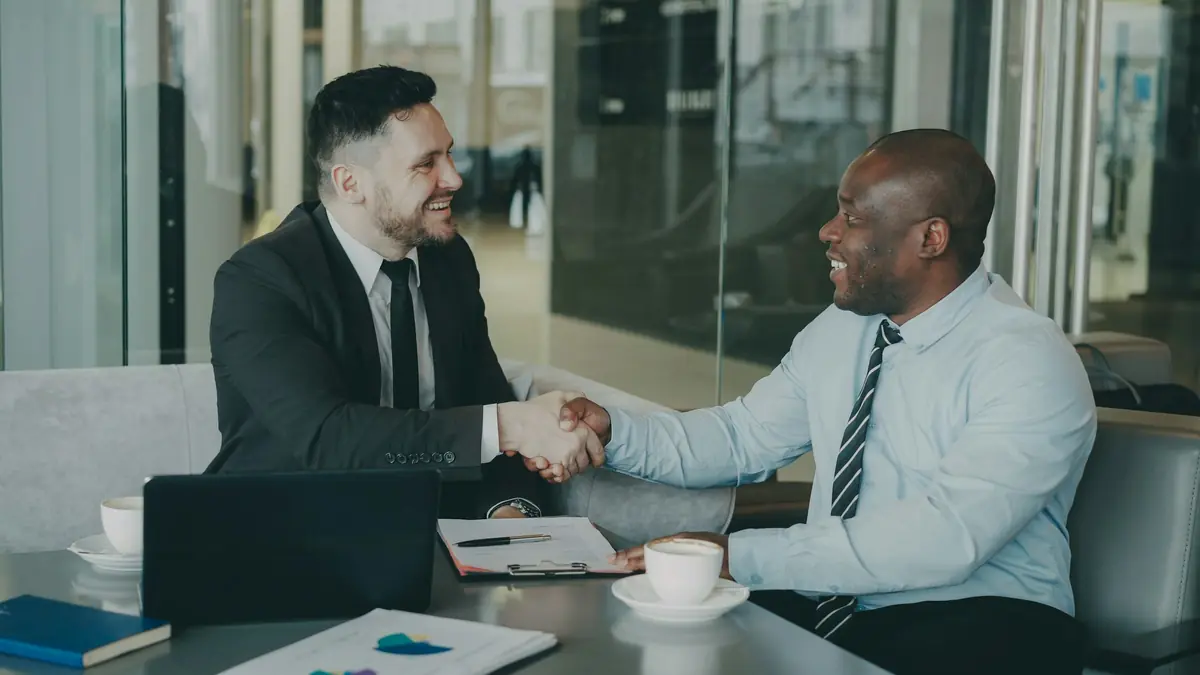 Two business people shaking hands across a table after agreeing a deal